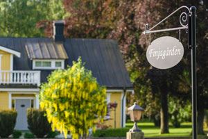 Finjagården Färgbild på ett gult hus med gröna buskar runt om kring och en skylt i förgrunden med texten Finjagården